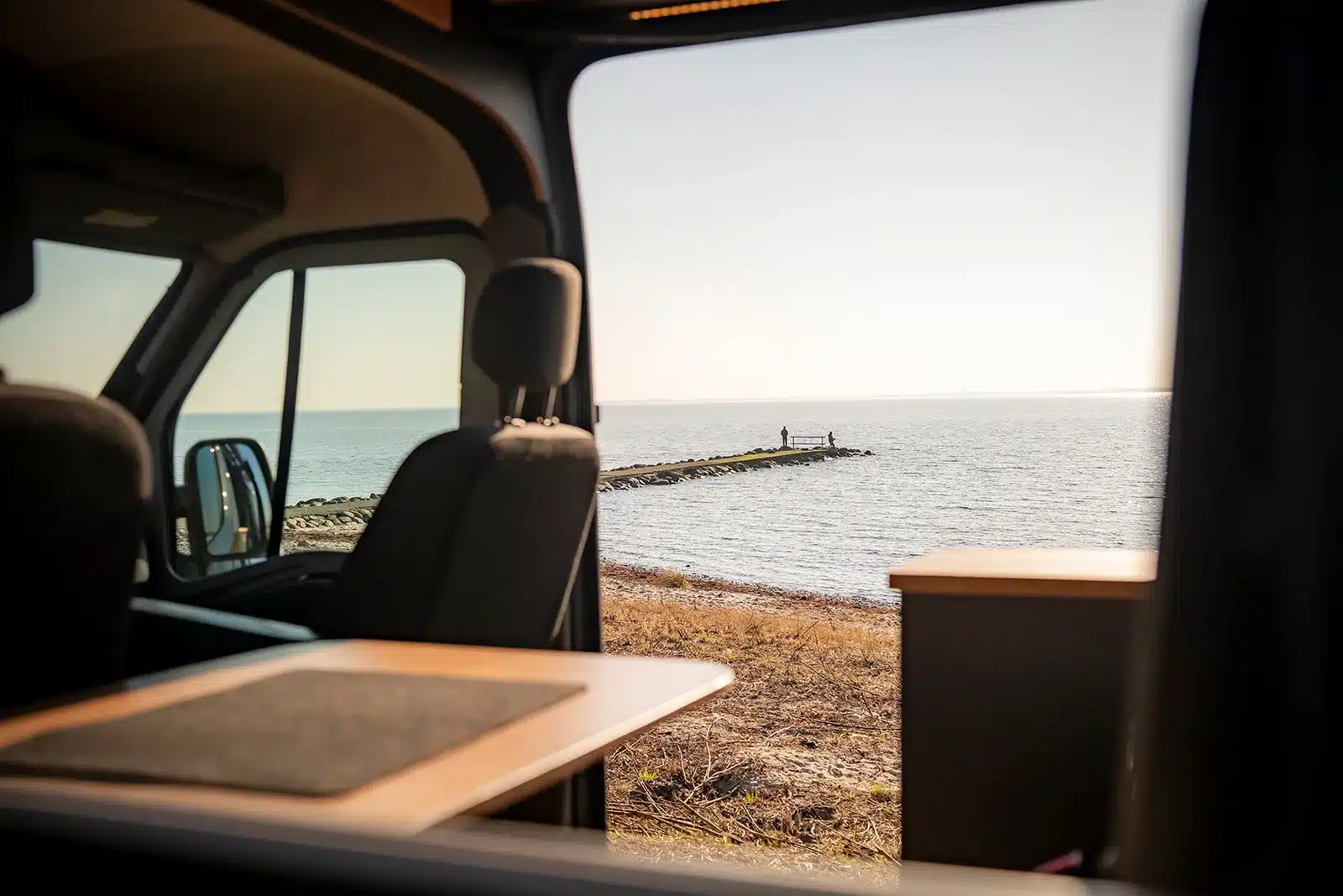 Blick aus dem Innenraum des Renault Master VANtastic auf das Meer mit Steg und zwei Personen