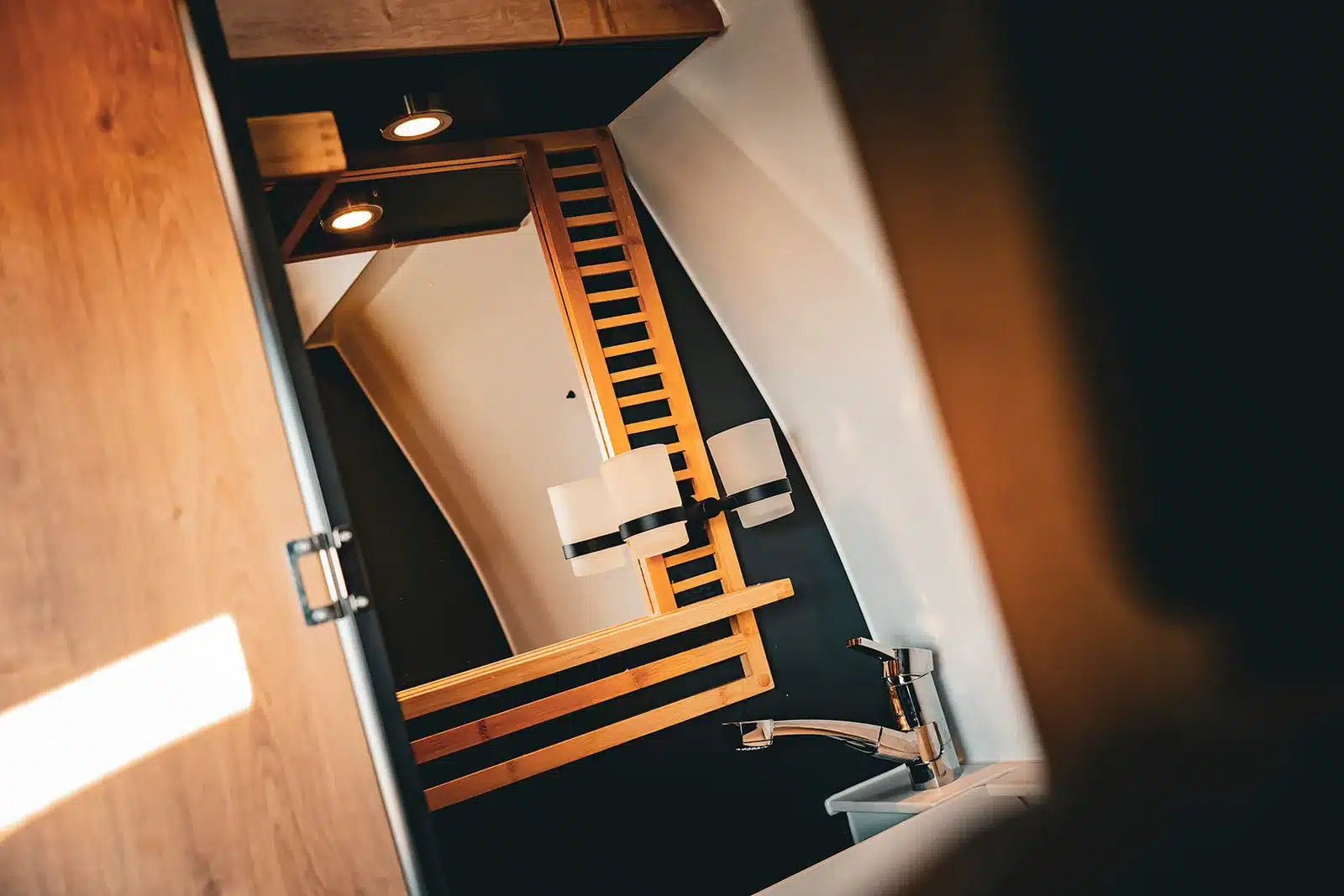 Badezimmer des Renault Master VANtastic mit Spiegelschrank, Waschbecken und stilvollen Holzelementen.