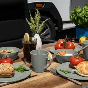 Camping-Geschirrset aus Polypropylen mit Tellern, Schalen und Bechern auf Campingtisch vor Campingfahrzeug