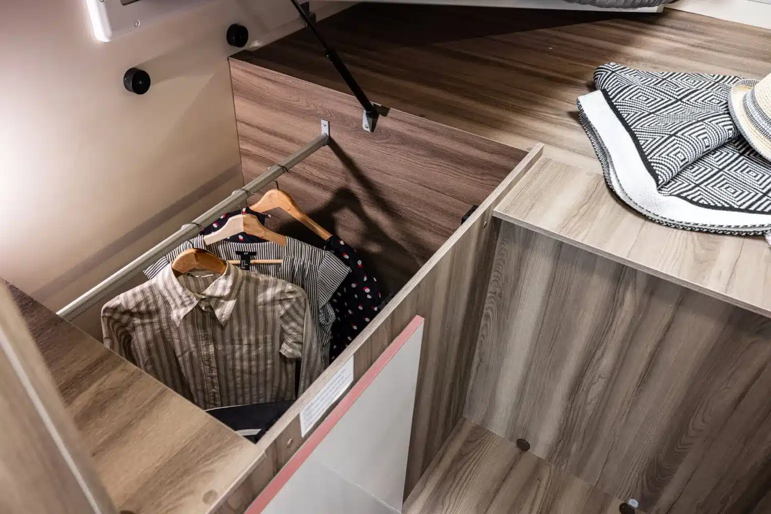 Kleiderschrank unter dem Bett im Kronos 285 TL Campingmobil mit hängender Kleidung und Decken.