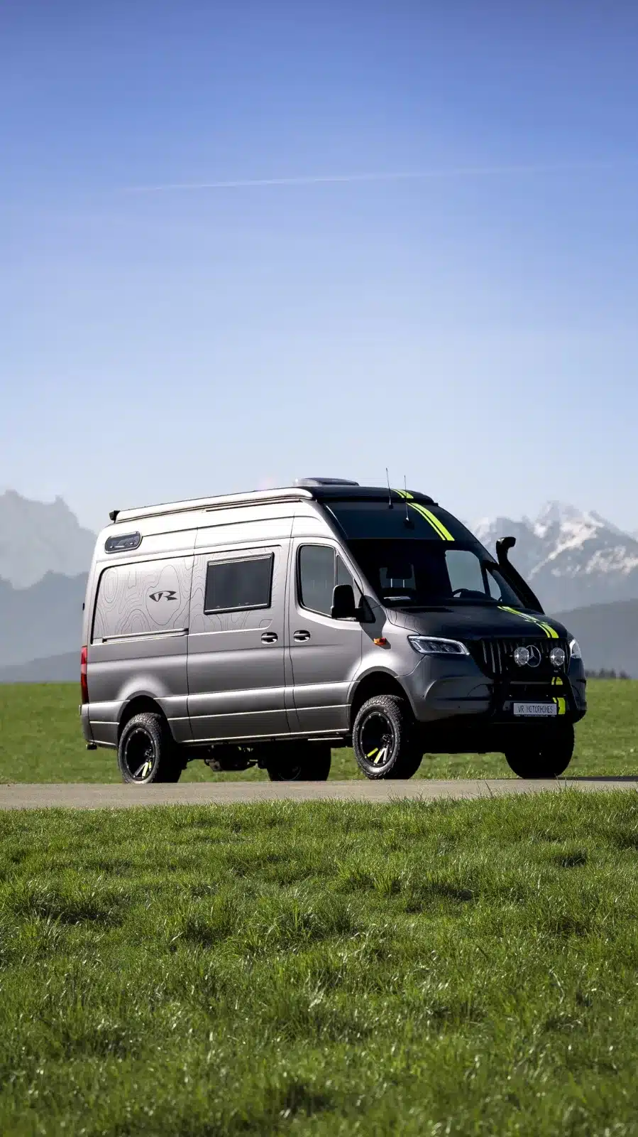 Silberner Mercedes-Benz Sprinter 6,0 m 4x4 von VR Motorhomes auf einer Wiese mit Bergen im Hintergrund