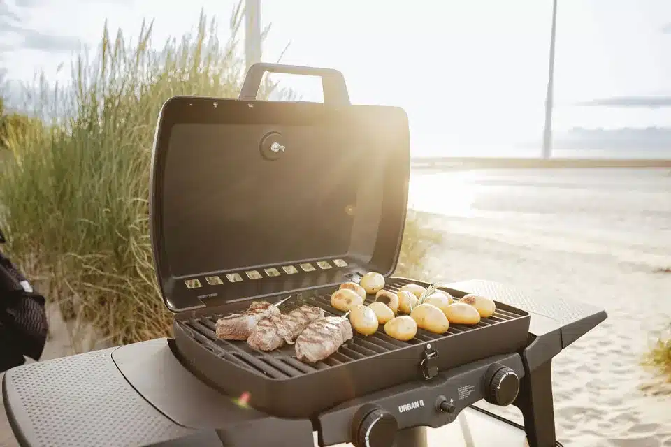 Geöffneter Enders Urban II Gasgrill mit Steaks und Kartoffeln auf dem Grillrost, aufgestellt am Strand
