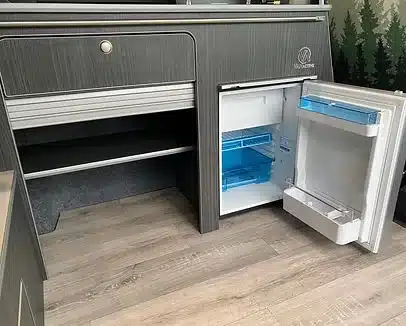 Küchenzeile mit geöffnetem 46-Liter-Kompressorkühlschrank und Stauraum im VA102 Premium Van-Ausbau.