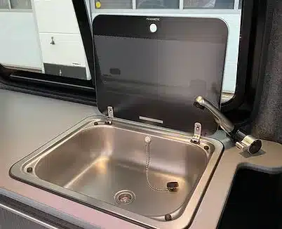 Dometic-Edelstahlspüle mit Glasabdeckung und Wasserhahn in einem Camper-Ausbau.