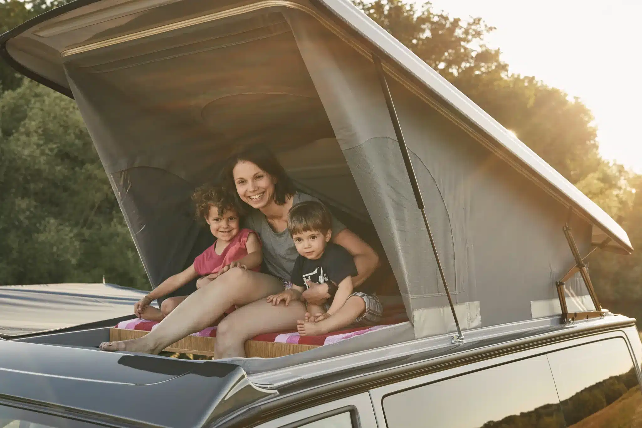 Familie entspannt im Aufstelldach eines VW T6.1 Campingbusses bei Sonnenuntergang