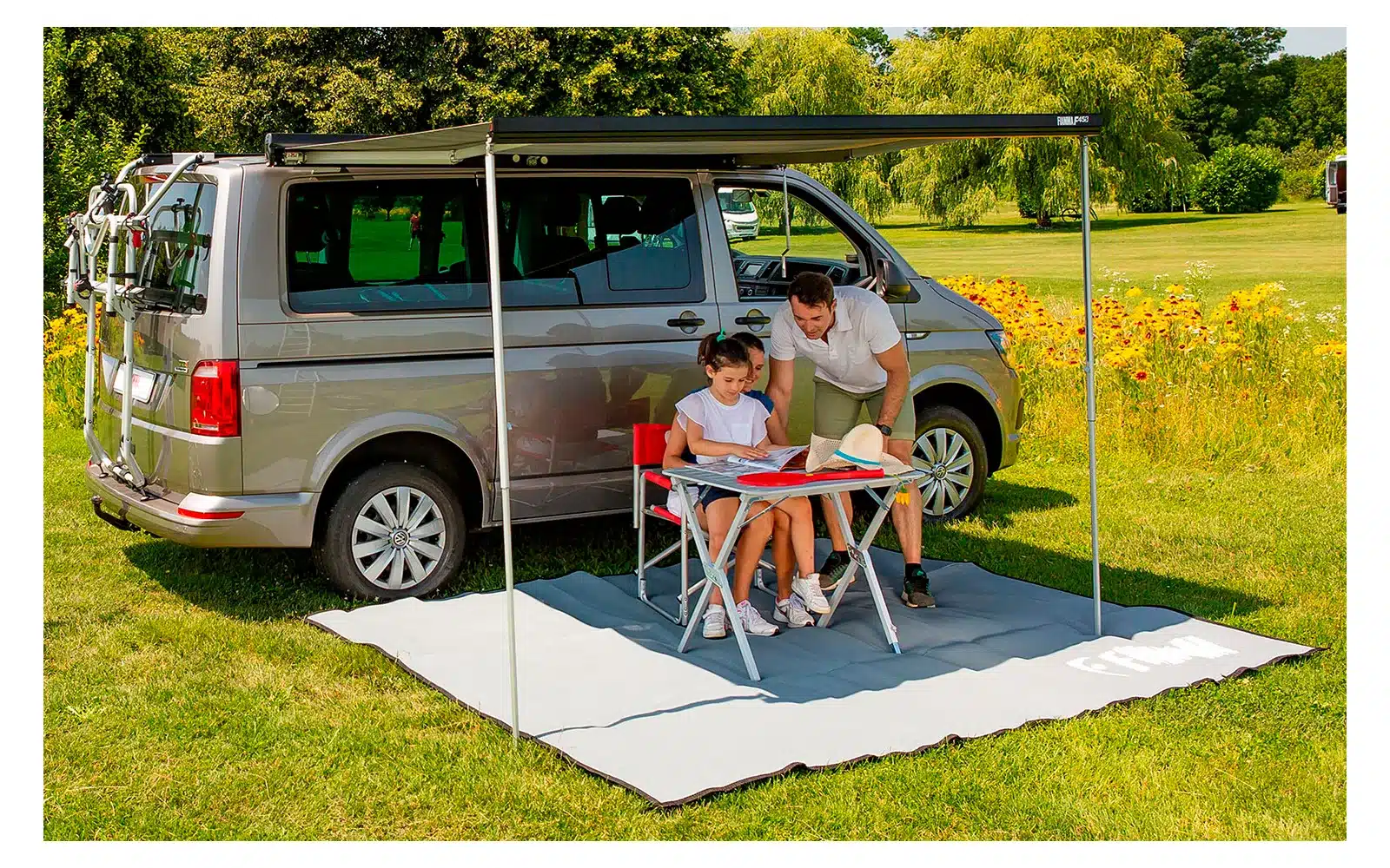 VW Bus T6 mit geöffneter Fiamma F45S Markise und Campingmöbeln auf einer Wiese
