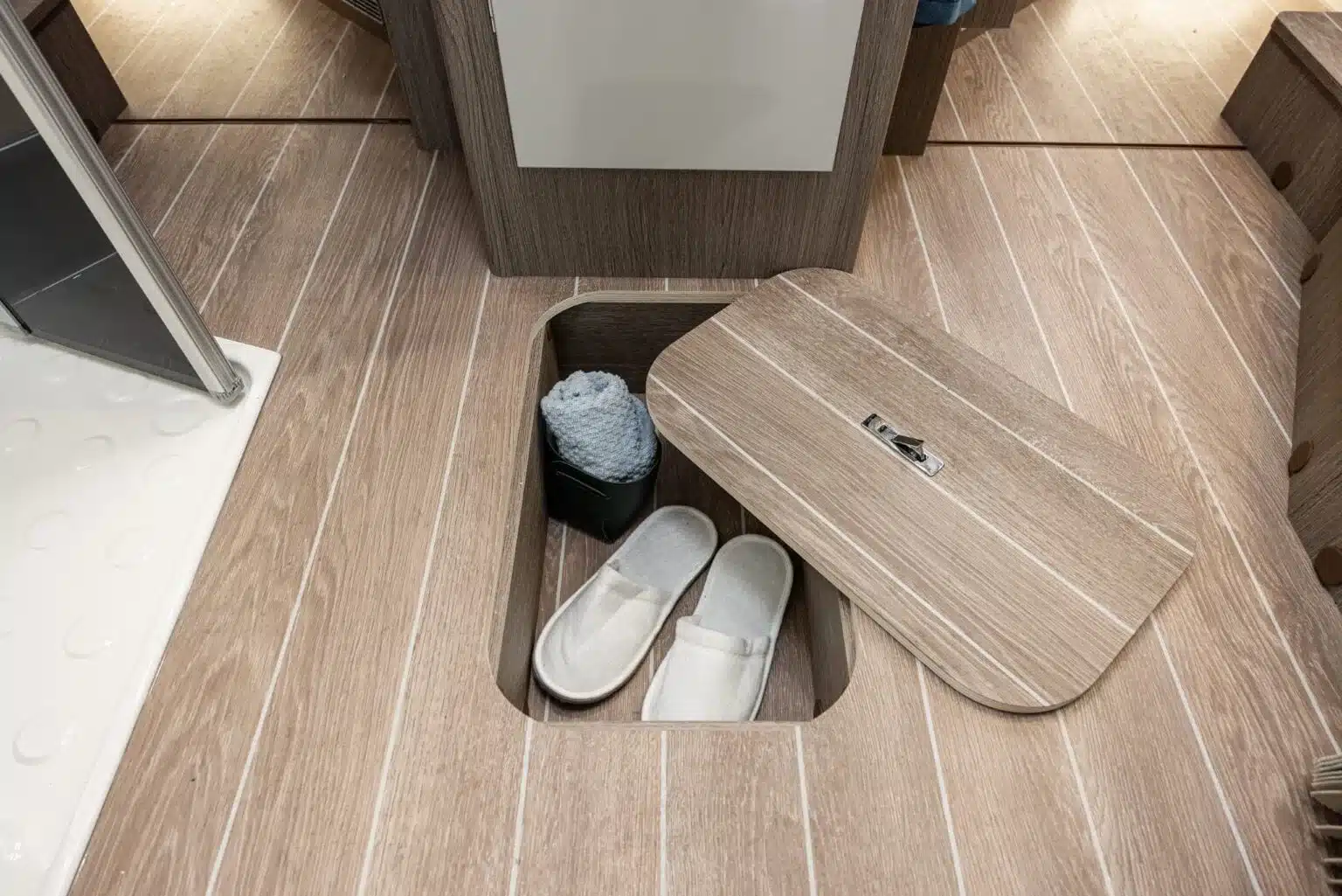 Bodenstaufach im Zefiro 266 TL POWER Edition mit geöffnetem Deckel, Hausschuhen und einem Handtuch