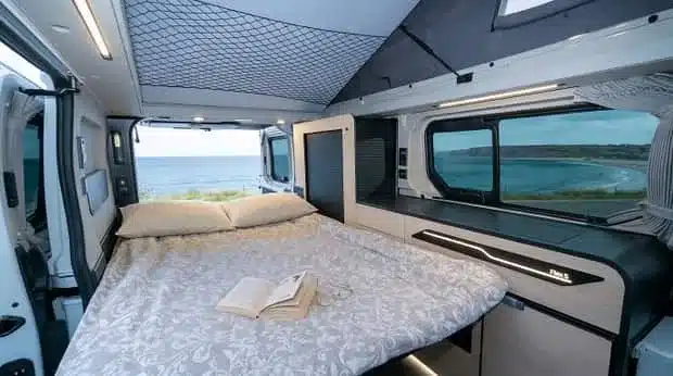 Innenraum des Antilope Van Flex 5 mit aufgebautem Bett und Ausblick durch das Fenster auf die Küste.