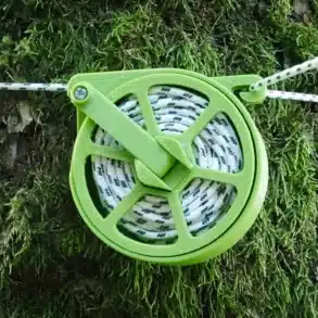 Auf einem Baum befestigte, aufgerollte Wäscheleine mit grünem Spulengehäuse für Camping und Vanlife