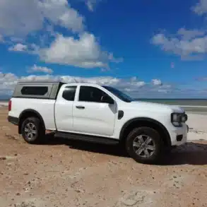 Weißen Pickup mit Contour Canopy am Sandstrand vor blauem Himmel und Meer.