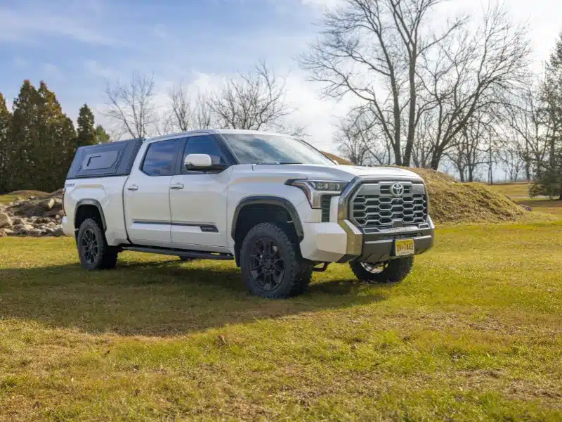 Weißer Pickup mit montiertem Contour Canopy Aufbau auf einer offenen Grasfläche bei Tageslicht.