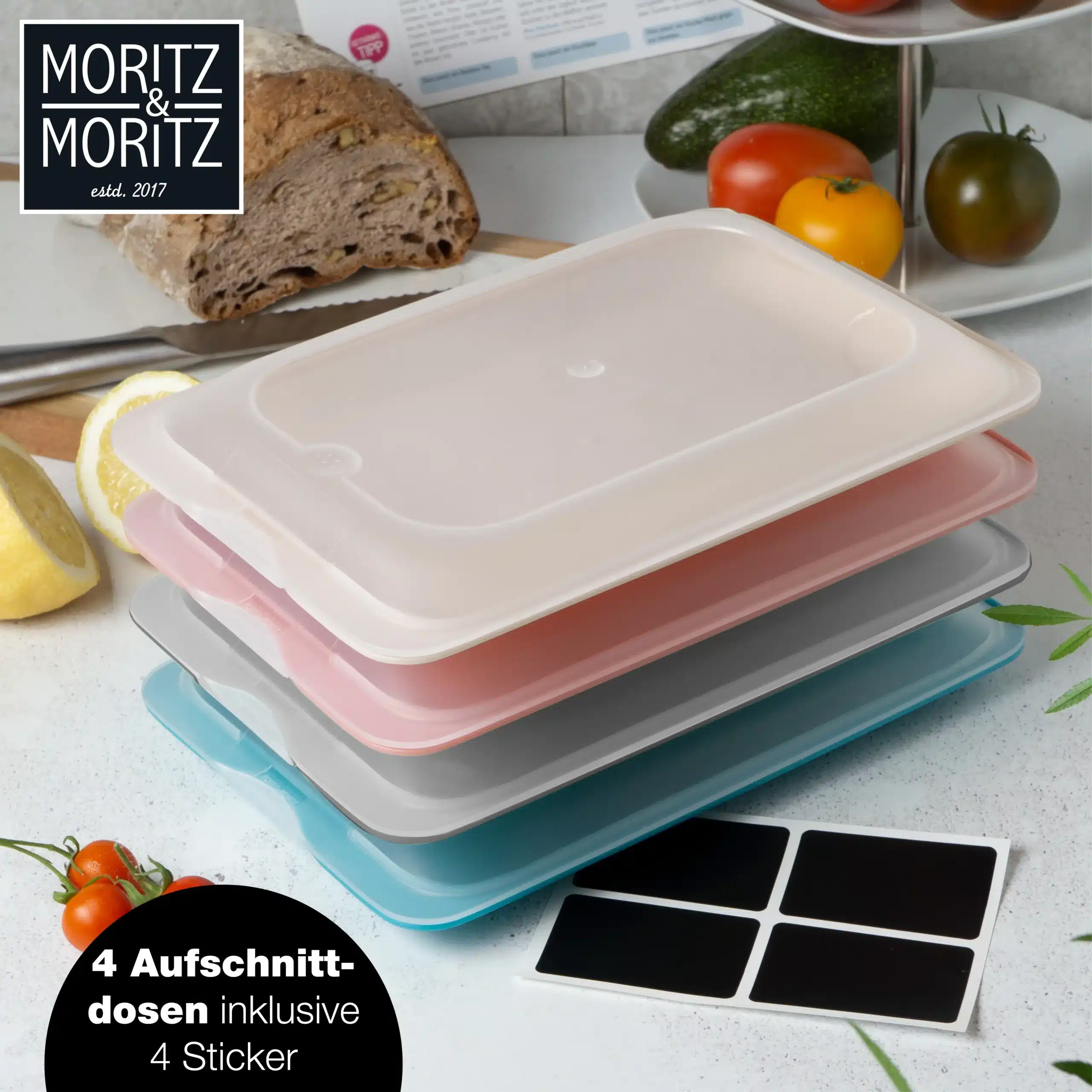 Vier flache, farbige Aufschnittdosen von Moritz & Moritz mit Tafelstickern auf einer Küchenarbeitsfläche, umgeben von Lebensmitteln.