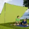 Zwei Personen liegen unter einem grünen Berger Sonnentarp auf einer Wiese am See und genießen den Schatten.