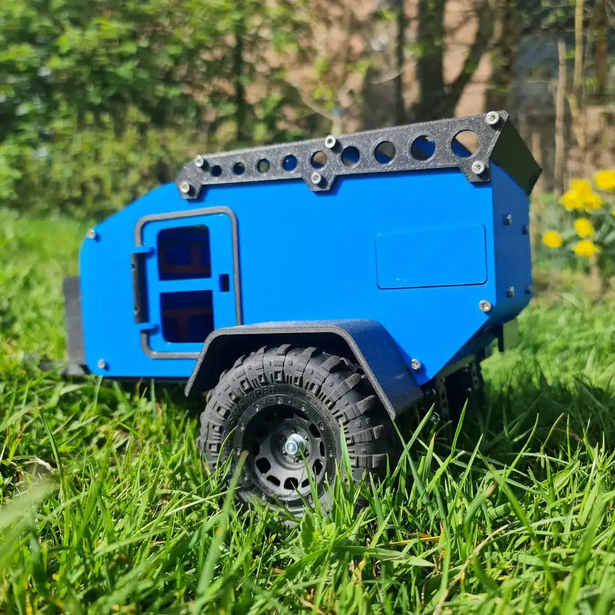 Modell eines blauen 3D-gedruckten Mini-Campers mit schwarzen Reifen im Gras