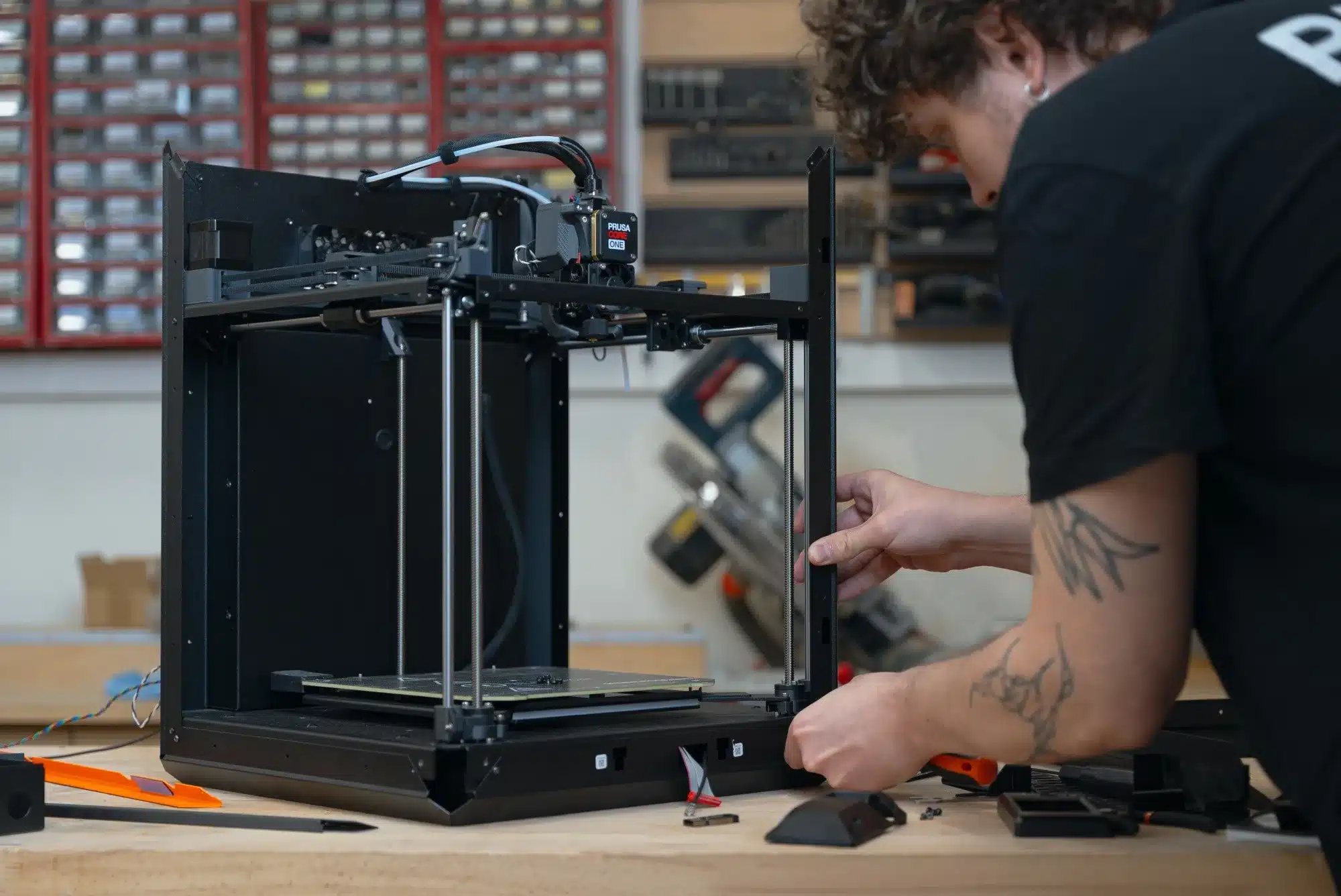 Person baut einen Prusa Core One+ 3D-Drucker an einer Werkbank zusammen