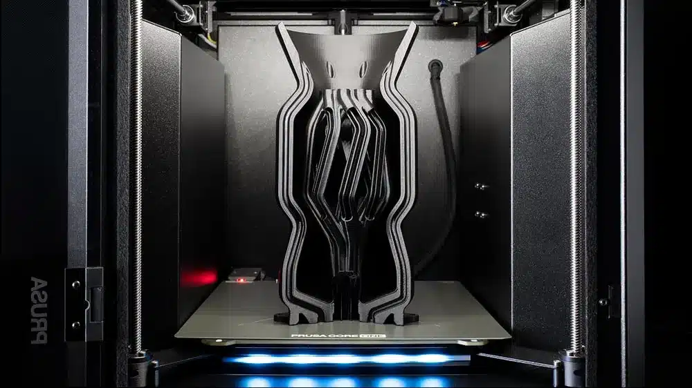 Blick in den Prusa Core One+ 3D-Drucker mit großem schwarzen Druckteil auf der Druckplatte.