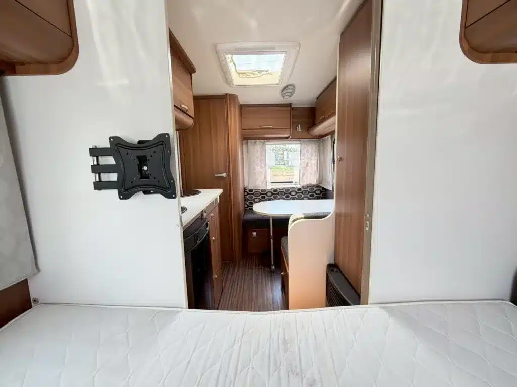 Innenansicht Wohnwagen Adria Altea 390PS: Bett, Küchenzeile und Sitzgruppe mit Holzdekor.