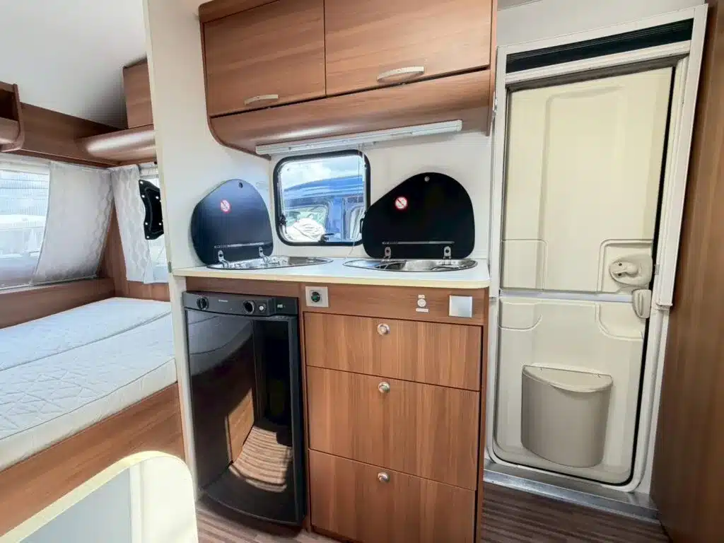 Innenansicht der Küche mit Spüle, Kocher, Kühlschrank und Stauraum im Adria Altea 390PS Wohnwagen