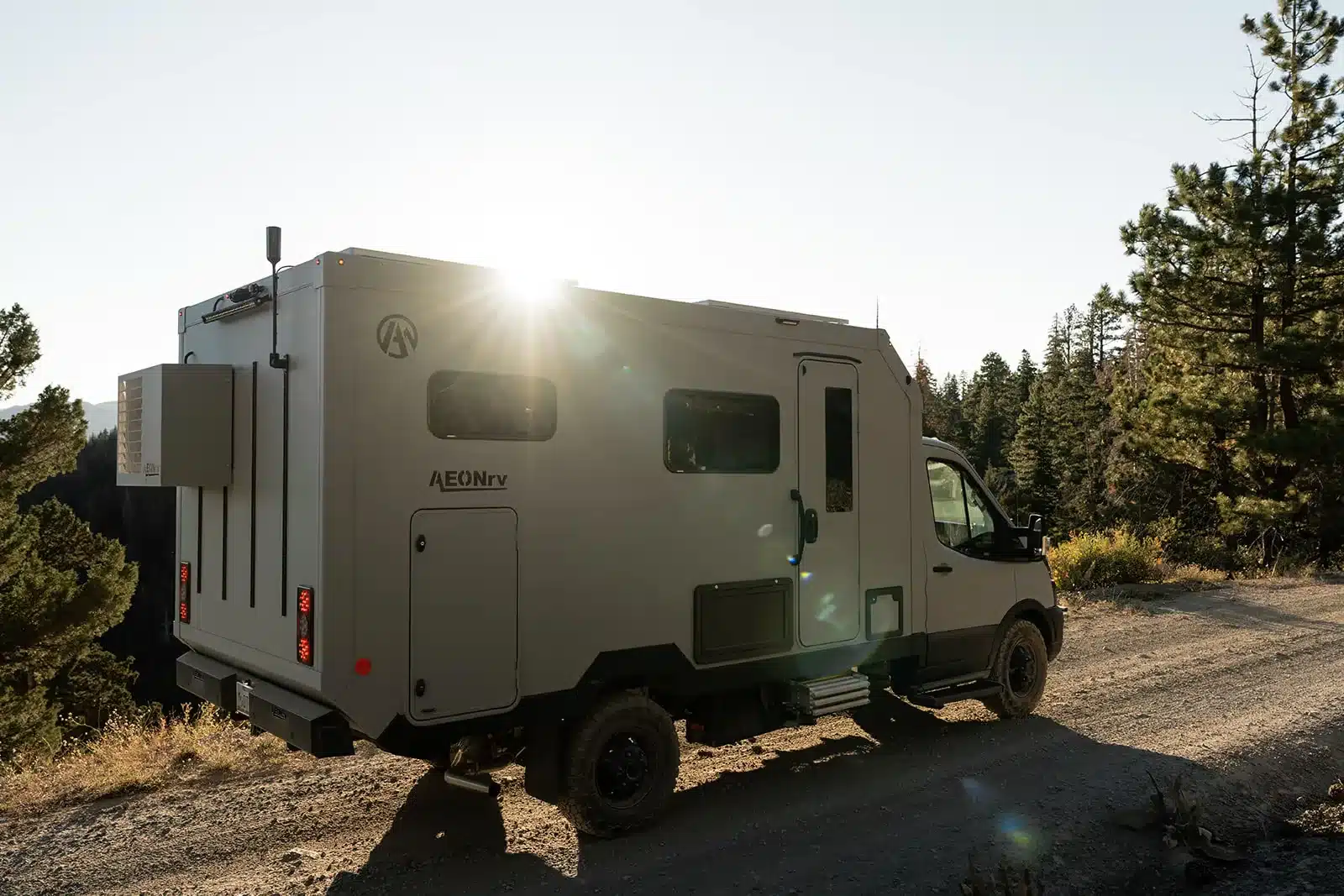 Der AEONrv Expeditions-Camper auf einer Schotterstraße im Abendlicht, umgeben von Bäumen.