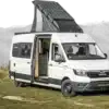 ALTIPLANO LONG Kastenwagen auf MAN TGE mit Solarpanel auf dem Dach und geöffnetert Seitentür, vor Alpenpanorama.