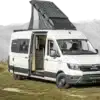 Altiplano Campervan MAN TGE L4 mit Solardach und offenem Einstieg auf einer Wiese vor Bergkulisse.