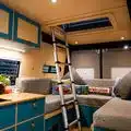 Innenraum eines Camper-Vans mit blauen Schränken, gemütlicher Sitzecke und Leiter zur Dachluke