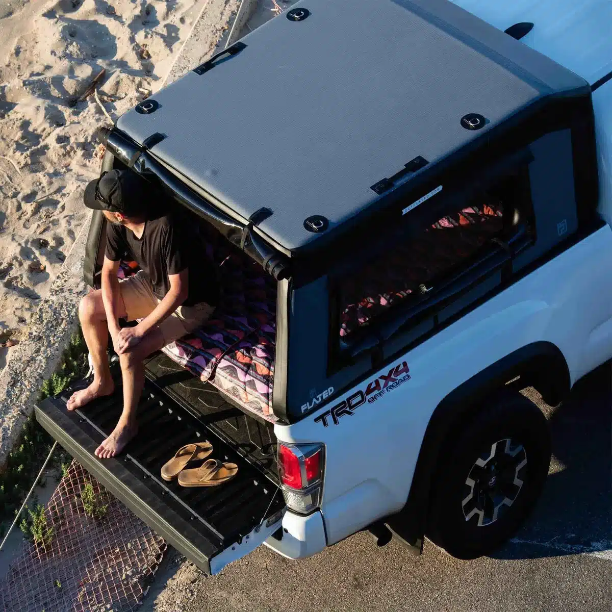 Pick-up mit aufgesetztem FLATED Air-Topper MR60 und Mensch am Strand, geöffnetes Heck, Blick von oben.