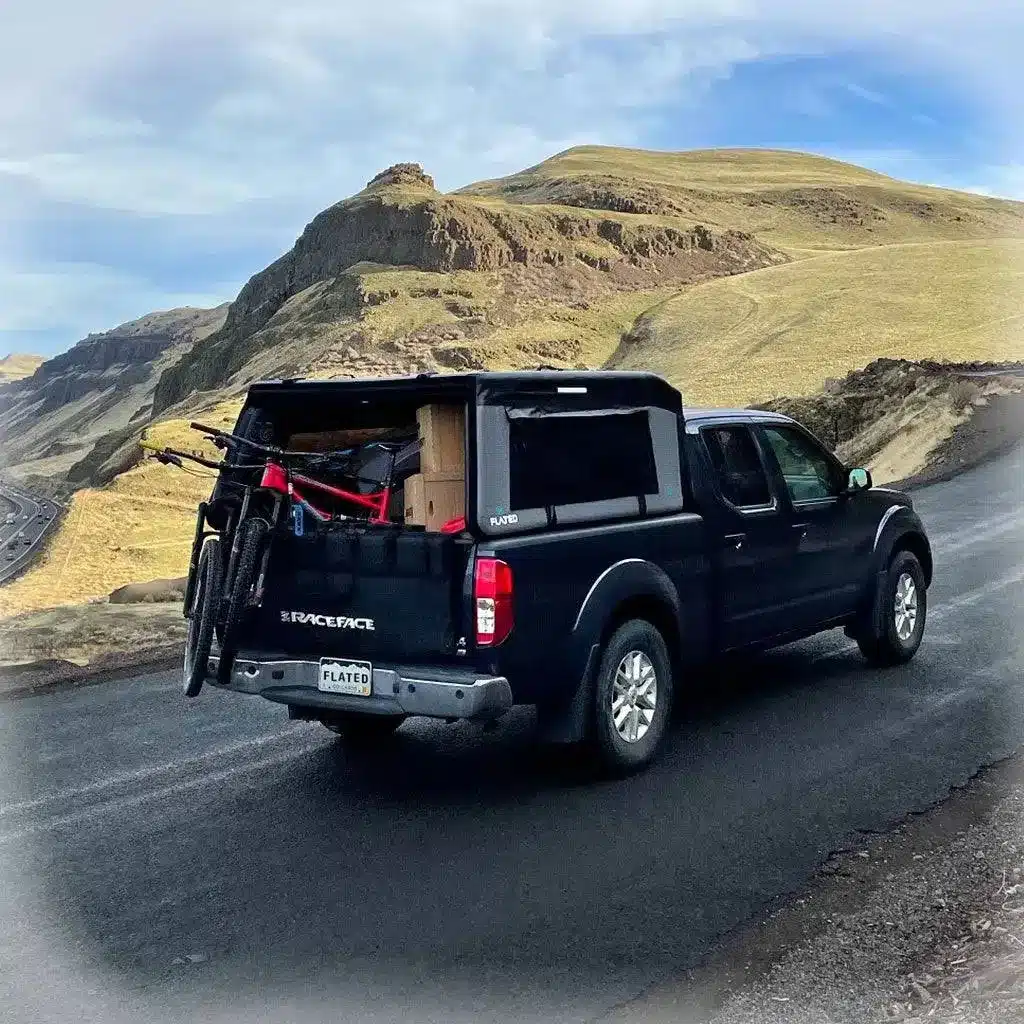 Mid-Size-Pick-up mit montiertem FLATED Air-Topper MR60 in bergiger Landschaft, Fahrräder am Heck.