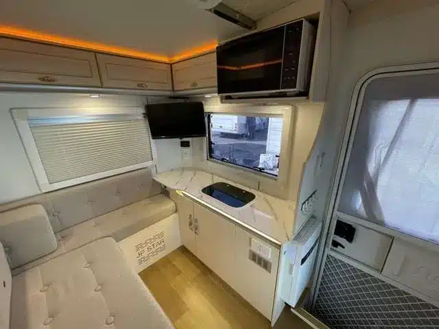 Blick in den modernen Innenraum eines JPSTAR Happy1+ Kei-Campers mit Sitzbank, Küchenzeile, Mikrowelle und TV