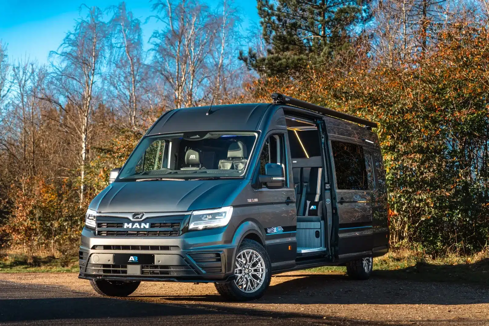 MAN TGE 180 Wohnmobil mit geöffneter Schiebetür auf einem Parkplatz am Waldrand