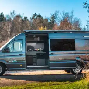Seitenansicht eines MAN TGE 180 Campervans mit geöffneter Schiebetür, sichtbarer Küchenzeile und Outdoor-Umgebung.