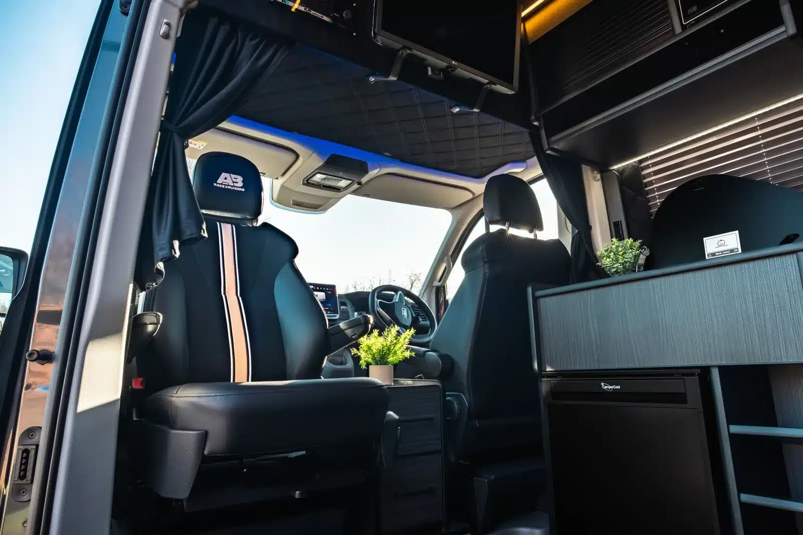 Modernes Fahrerhaus und vorderer Wohnbereich eines ausgebauten MAN TGE 180 Campers mit schwarzen Ledersitzen und Küchenelementen