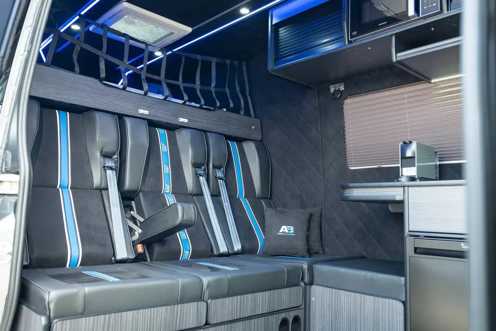 Wohn- und Sitzbereich im Mercedes Sprinter Race-Van mit Dreiersitzbank, Tisch, Kühlschrank und Mikrowelle