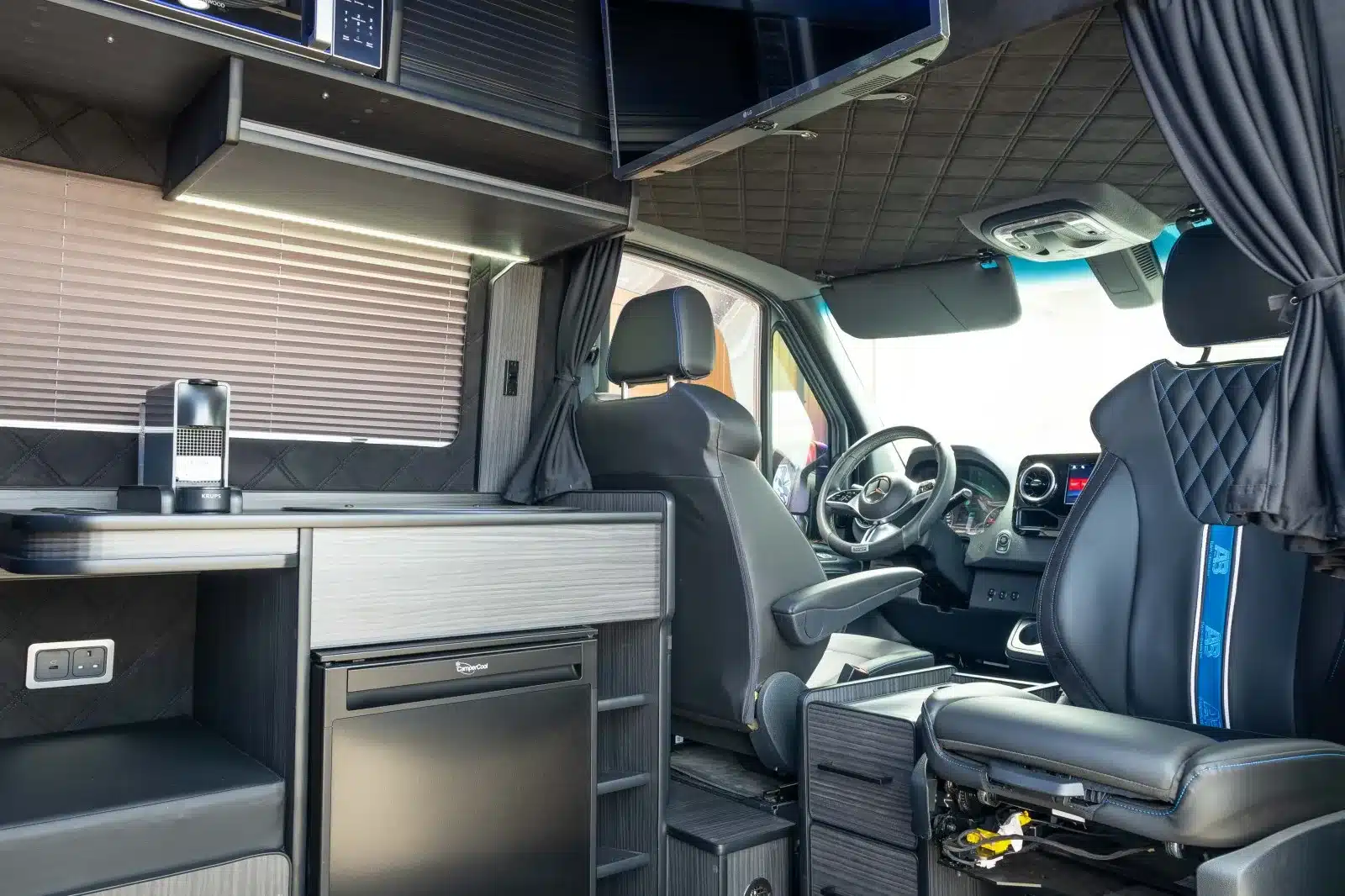 Innenraumansicht eines umgebauten Mercedes Sprinter 319 V6 mit Küchenzeile, Fahrerhaus und Sitzbank.