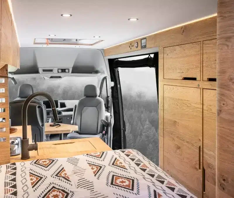 Blick in den Innenraum des Ontario Vans mit festem Heckbett, Stauraum, Sitzgruppe und Holzeinbauten.