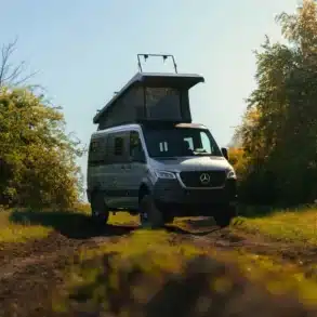 Kastenwagen Sportive mit Aufstelldach auf einem Feldweg, umgeben von Bäumen