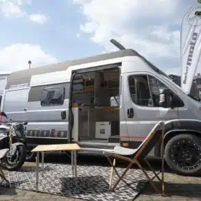 Rocket Moto Kastenwagen mit geöffneter Tür, Motorrad und Campingstühlen auf dem Stellplatz