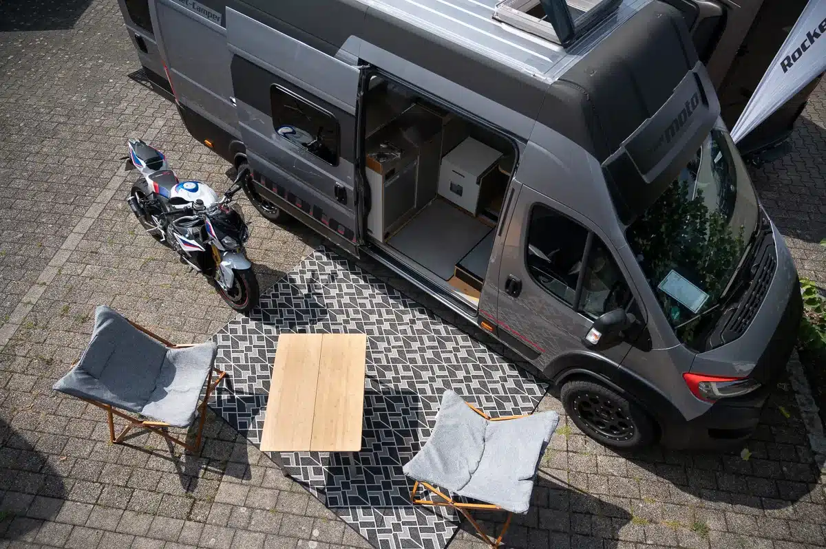Ansicht eines Rocket Moto Campingvans mit offenem Eingang, Motorrad und aufgebauter Campingfläche