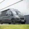 Rocket One L 2.4 P Campervan in Seitenansicht vor moderner Industriehalle, kompakter Wohnmobil-Kastenwagen mit Markise