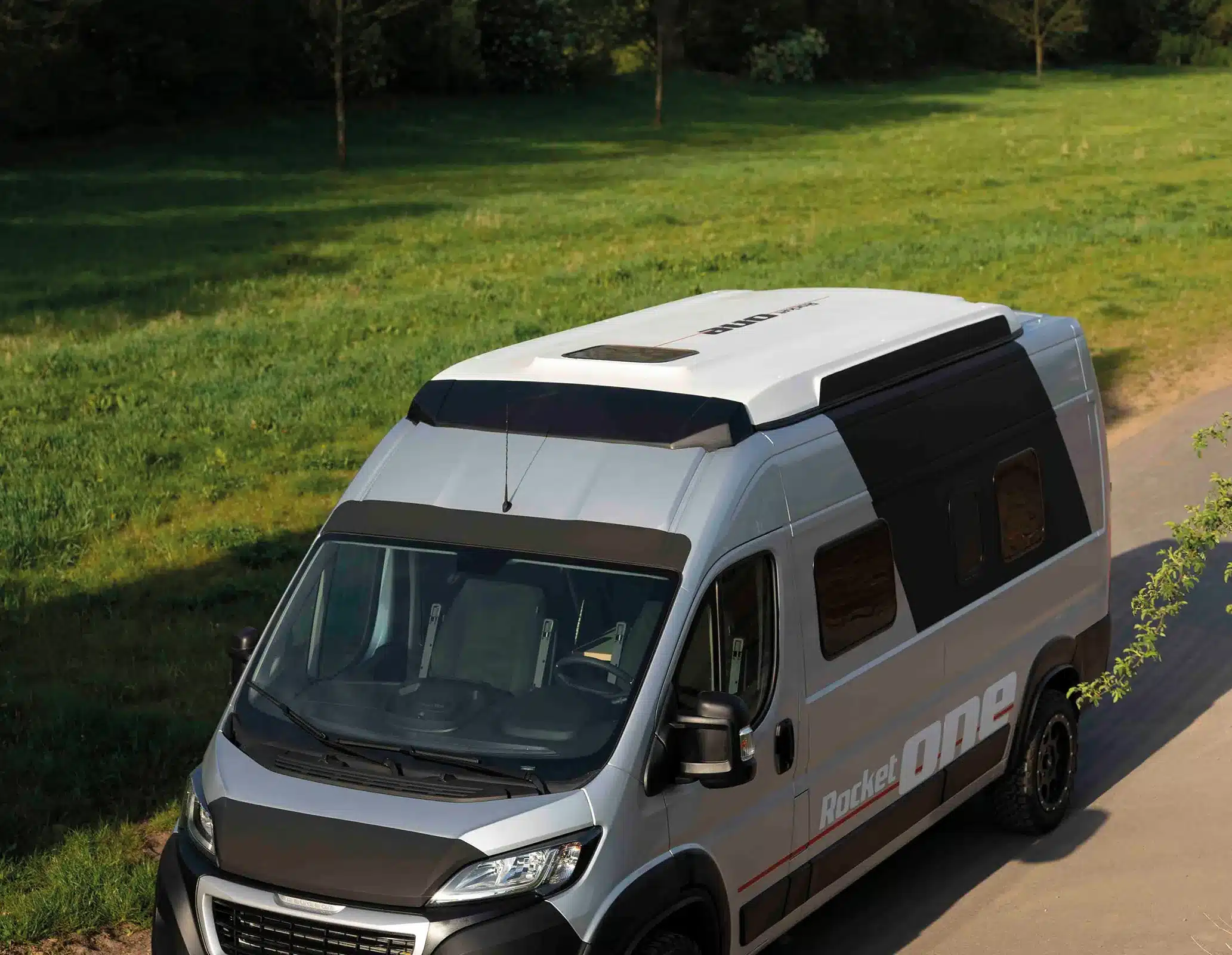 Campervan ROCKET ONE M mit Hochdach und seitlicher Beschriftung auf einer Landstraße aus der Vogelperspektive.