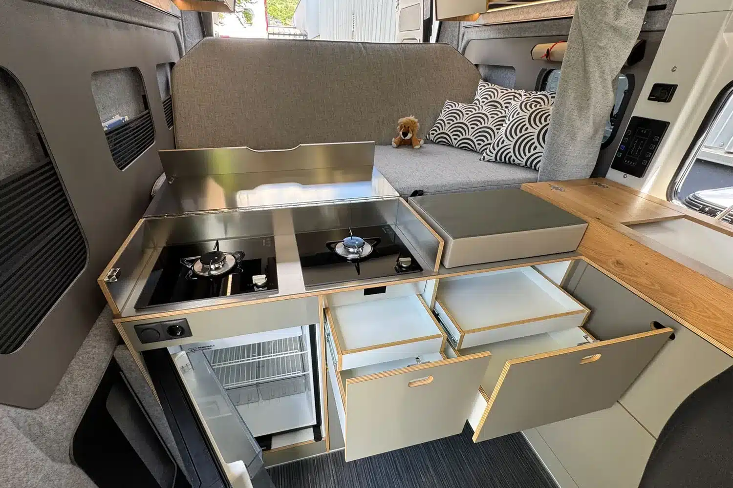 Innenaufnahme der ROCKET ONE M Campervan-Küche mit offenem Gasherd, Kühlschrank und Schubladen