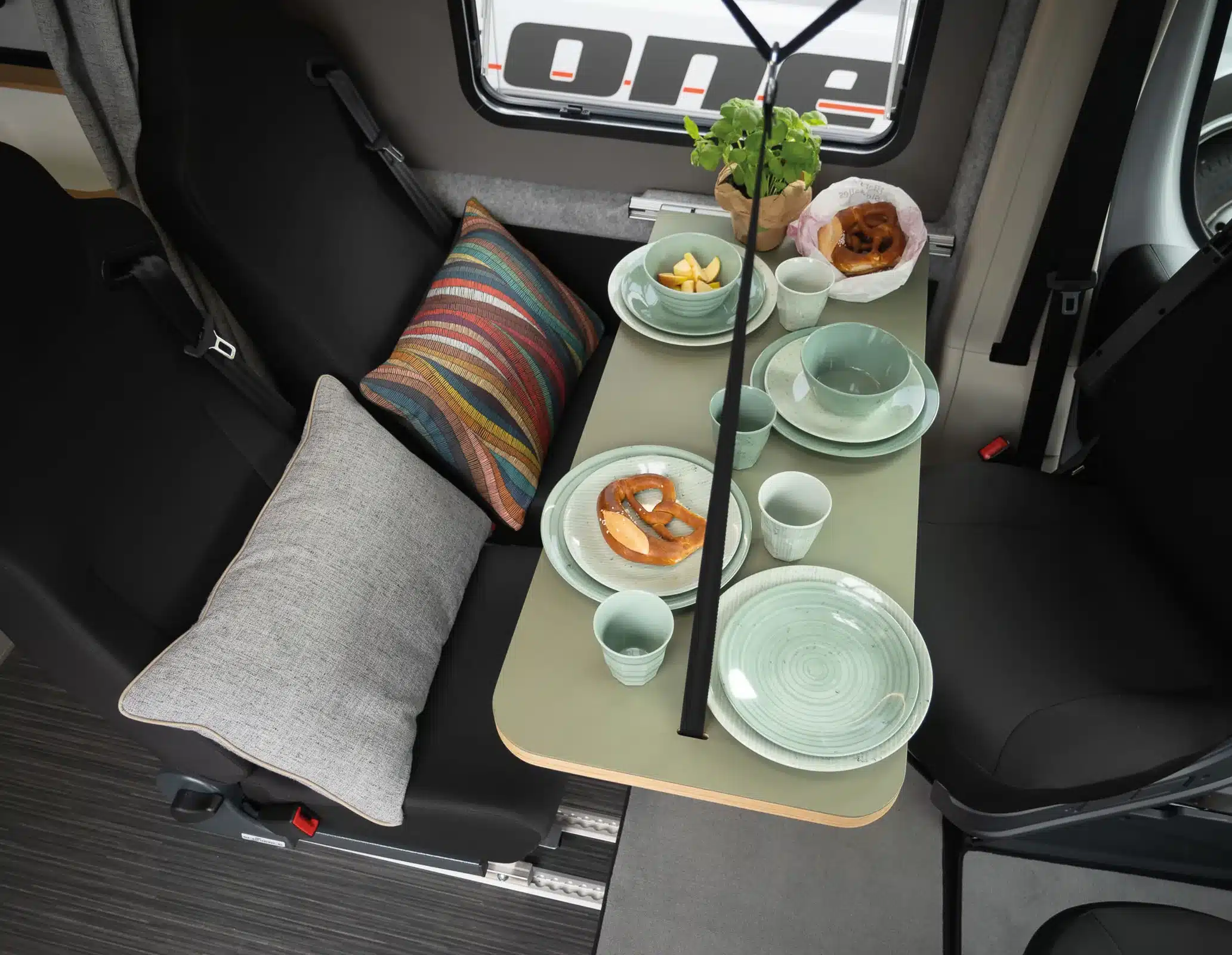 Essbereich und Sitzgruppe im Rocket One XL mit gedecktem Tisch, Geschirr und Polsterkissen.