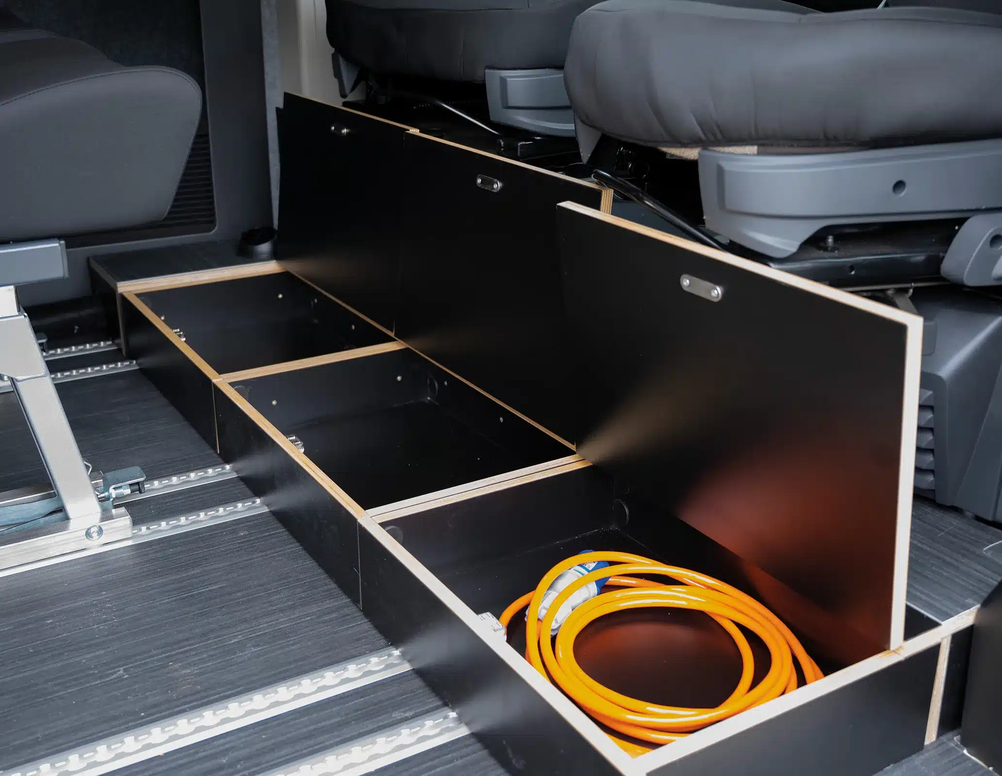 Offene Staufächer im Boden des Rocket One XL Kastenwagens mit aufgewickeltem Stromkabel.