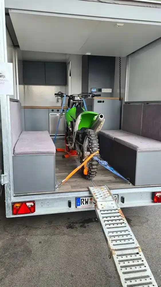 Innenraum eines Spikes-Caravan mit fest verzurrtem Motorrad und sichtbaren Sitzflächen.