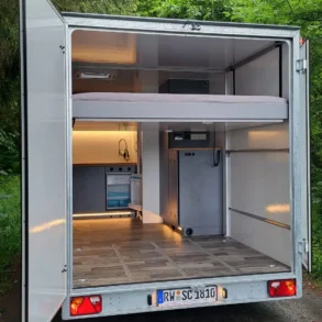 Modularer Innenraum eines geöffneten Spikes-Caravan im Grünen, mit Küche und Bett sichtbar