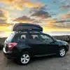 Auto mit FLATED SPORT CARRIER15 Dachbox bei Sonnenuntergang am Strand