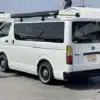 Toyota HiAce V Super GL Dark Prime II 2023 weiß, Rückansicht, mit Markise, auf einem Parkplatz.