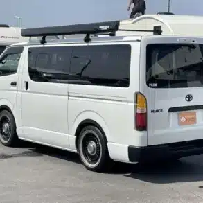 Toyota HiAce V Super GL Dark Prime II 2023 weiß, Rückansicht, mit Markise, auf einem Parkplatz.