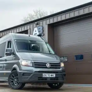 VW Crafter Race Cruiser 2020 in grau mit Alufelgen, vor einer Werkstatt geparkt.