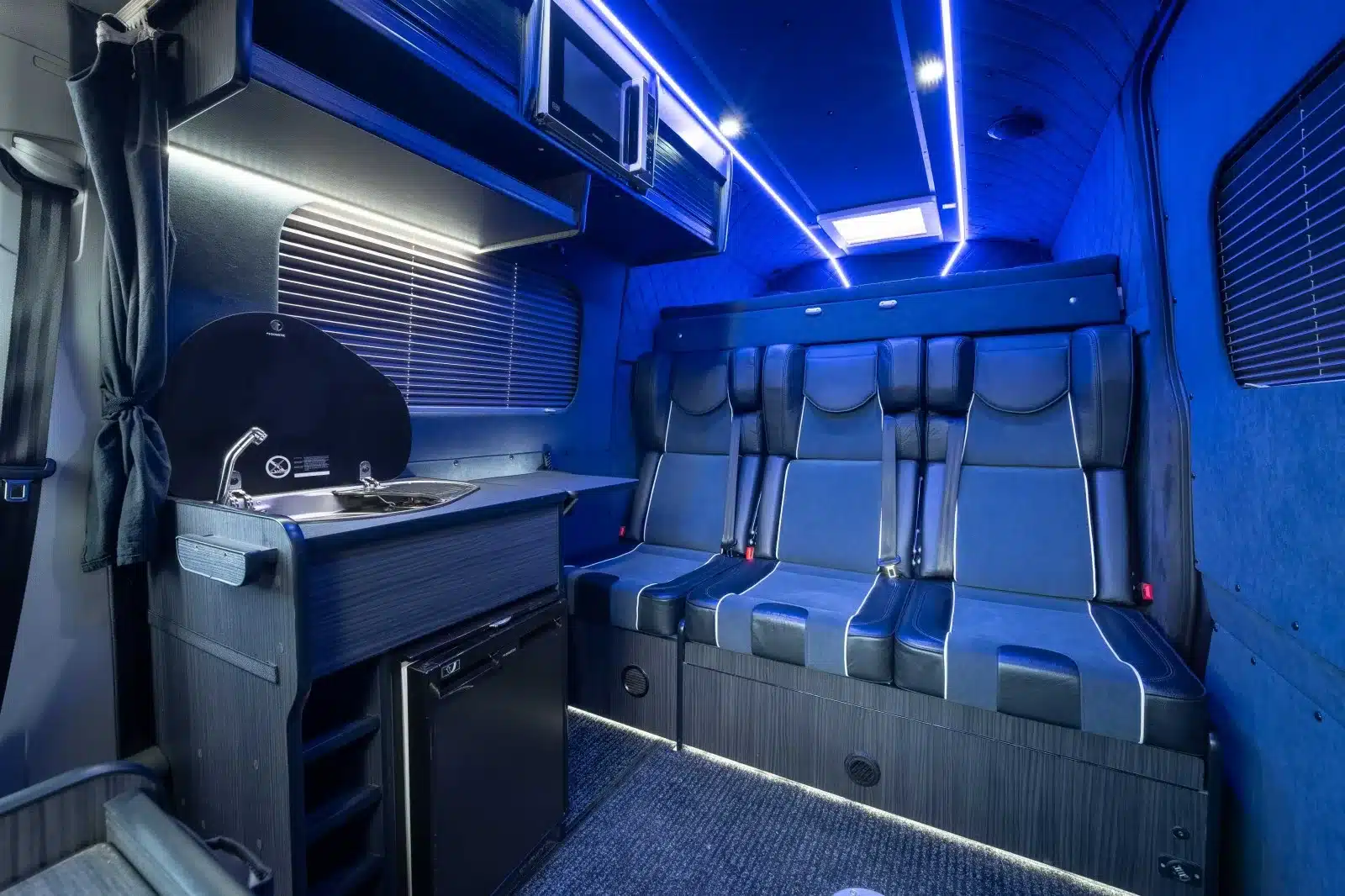 Innenansicht eines VW Crafter Race Cruiser mit Dreiersitzbank, Küchenzeile und blauer LED-Beleuchtung
